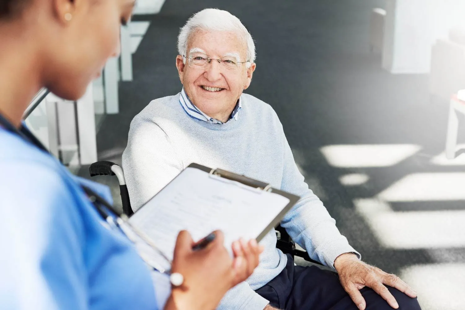 Smiling older man in glasses talking through his details with a nurse holding a clipboard